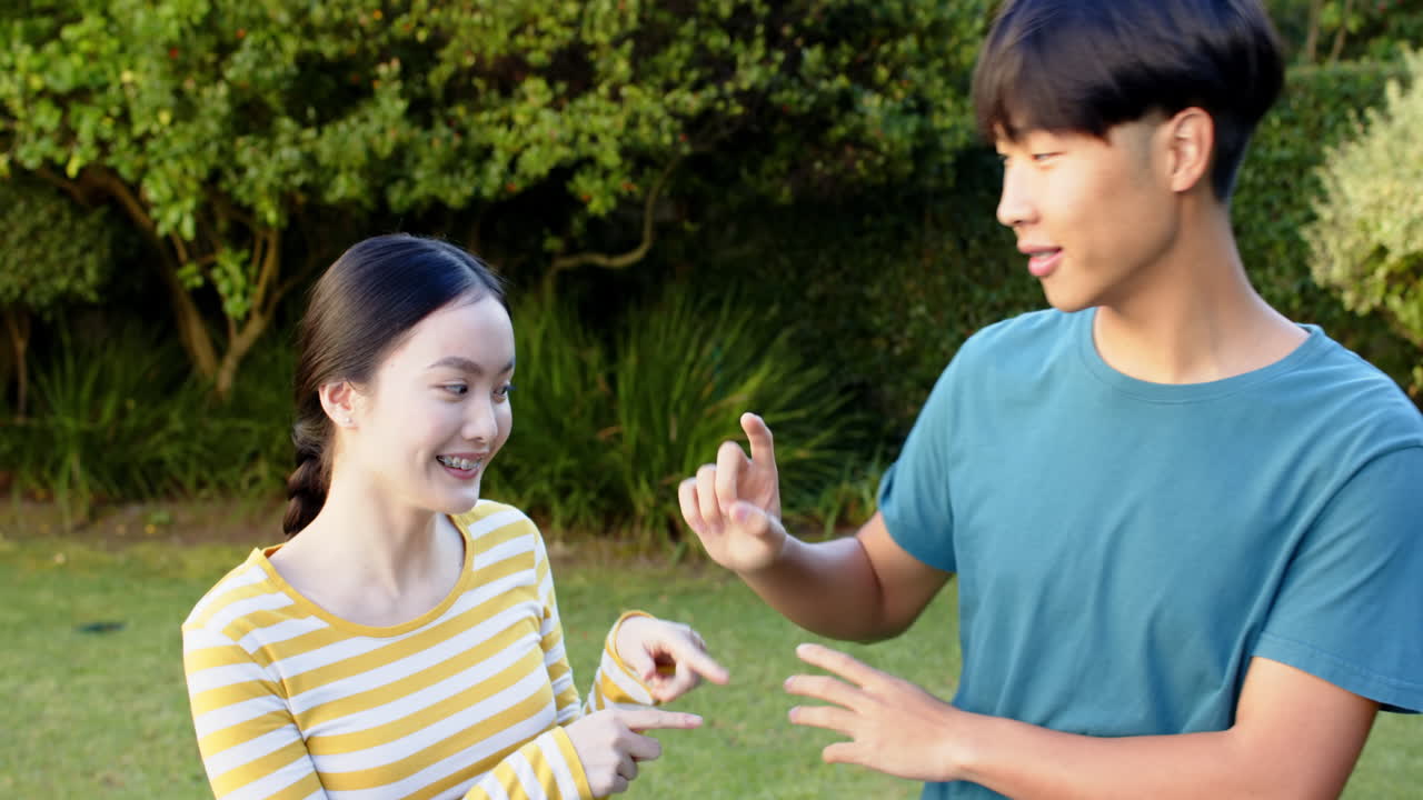 Smiling Asian brother and sister communicating using sign language in outdoor park setting
