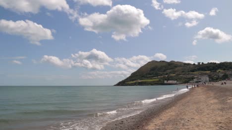 People-on-a-beach-on-a-sunny-day,-with-hills-and-houses-in-the-background