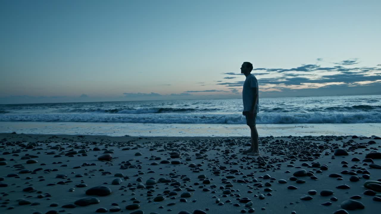 Silhouette of a person standing on a rocky beach at sunset, captured from a low angle