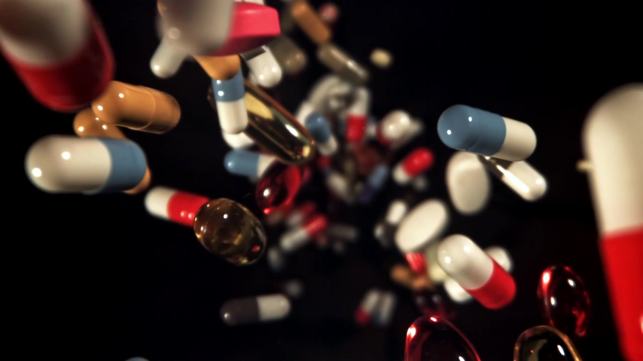 Pillole e capsule colorate che fluttuano al rallentatore su sfondo nero