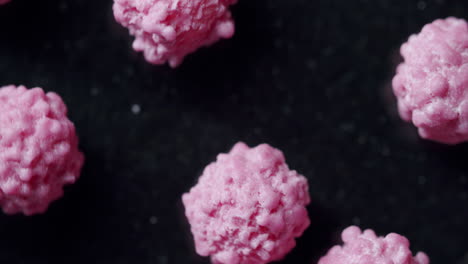 top shot of pink particles spinning clockwise on a dark surface. commercial side light from the left. particles looking like a virus or disease