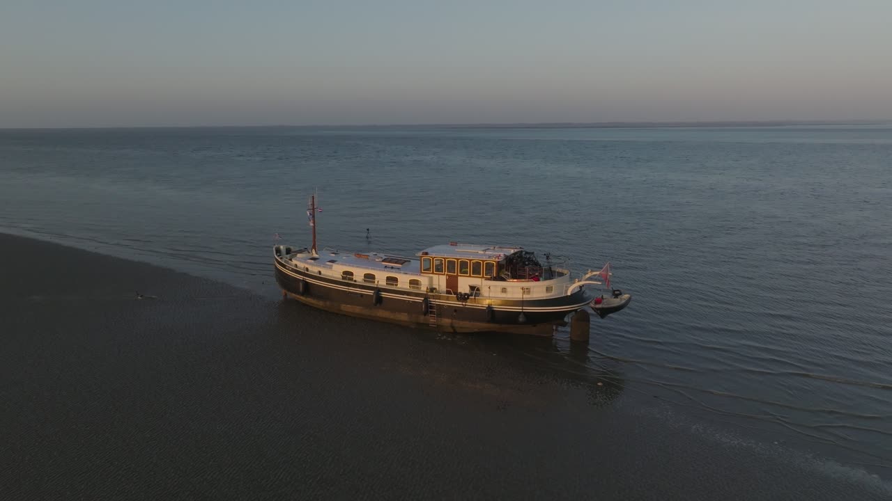 Wide scene with the Luxemotor boat on the flats under a low bright sun; gentle ripples on shallow water. Wadden Sea