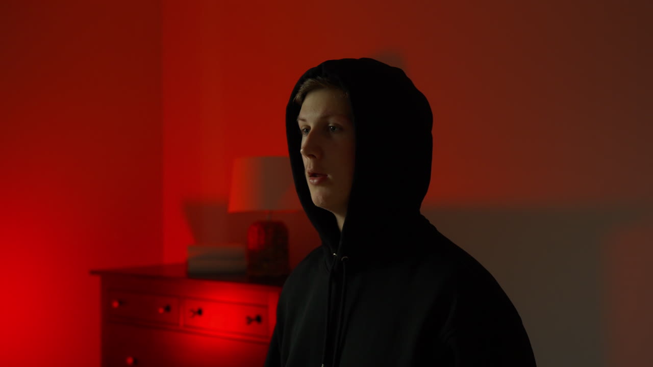 Close-up portrait of young hooded figure, expression reveals shock and panic, harsh red and blue light illuminates tense moment following alarm activation during illegal act, panic mood
