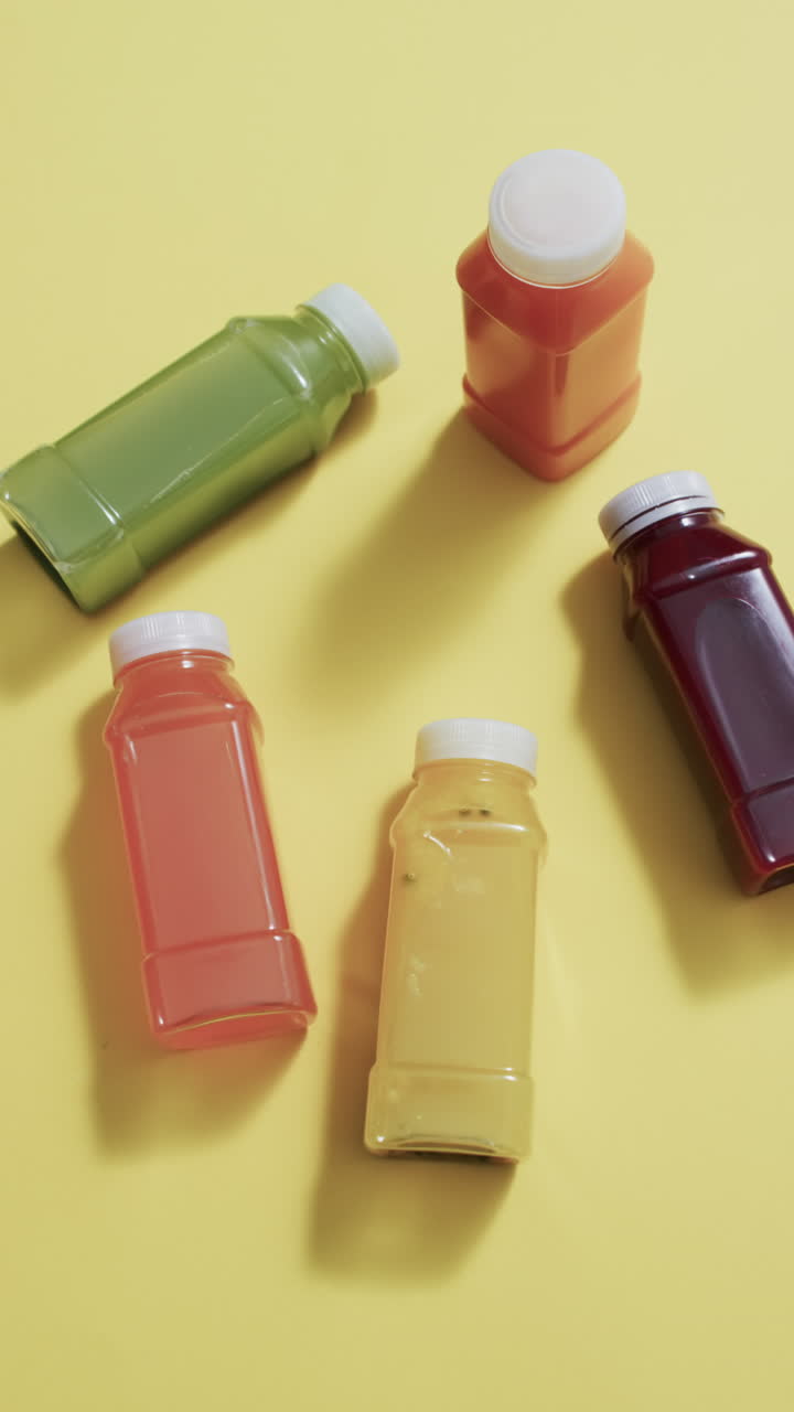 Vertical video of bottles of fruit juice with copy space over yellow background