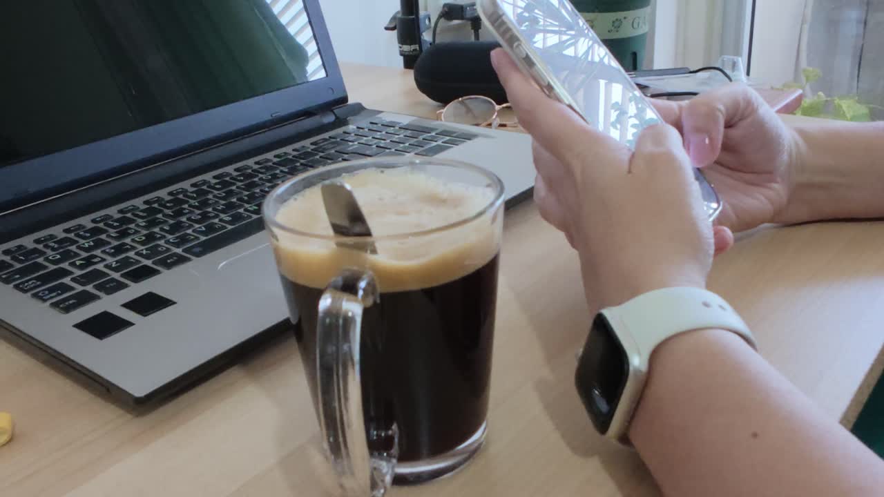 Primo piano delle mani di una donna che usa lo smartphone alla scrivania con laptop e caffè