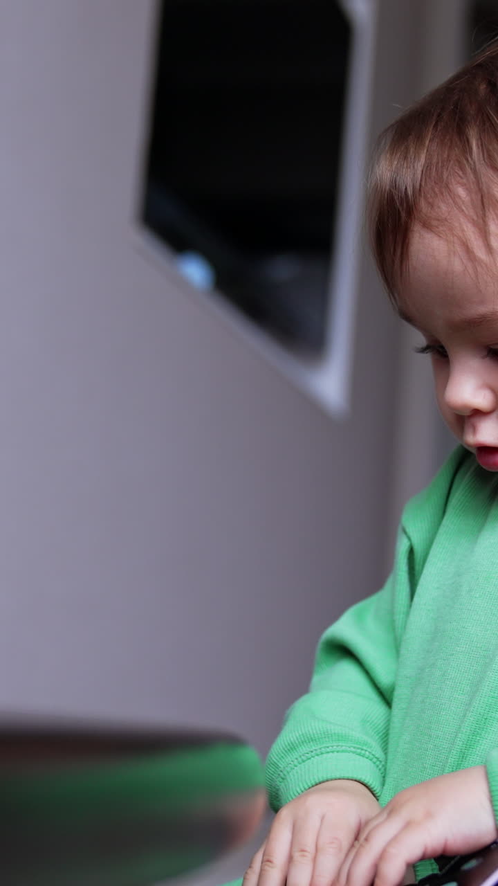 Brown-haired Caucasian baby boy dealing with phone. Little curious kid sits on the floor and explores gadget carefully. Close up. Vertical video