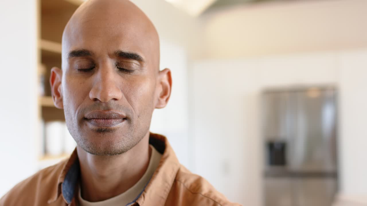 South Asian male blinking and reflecting in kitchen while shifting gaze toward shelves with mugs