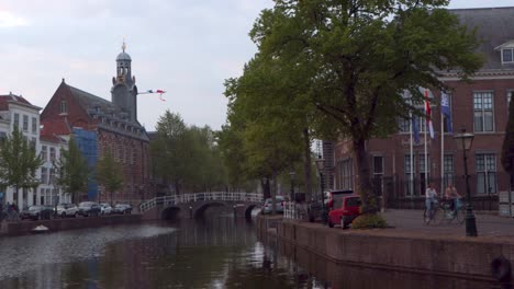 People-cycling-along-canal-in-city-in-the-Netherlands-on-national-holiday-King's-Day-during-coronavirus-pandemic,-with-Dutch-flags-in-background