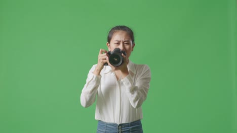 fotógrafo asiático enojado diciéndole al modelo que se mueva a la izquierda y a la derecha mientras toma fotos con la cámara en el fondo de la pantalla verde en el estudio
