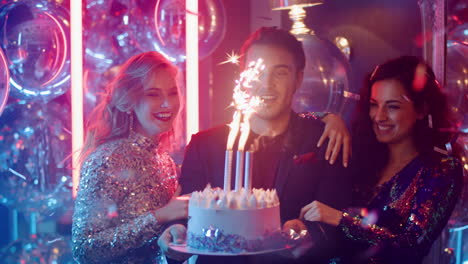 Cute-man-and-women-holding-cake-at-party.-Happy-friends-blowing-candles-in-club