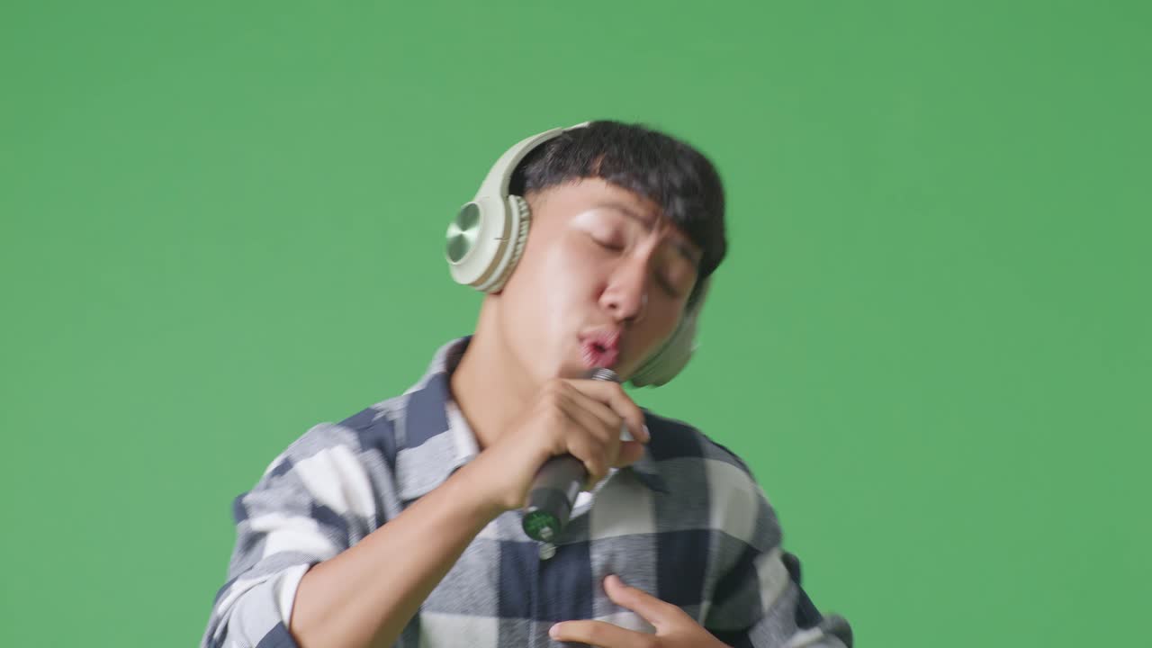 녹색 화면 배경에서 마이크를 들고 하는 젊은 아시아 십대 소년