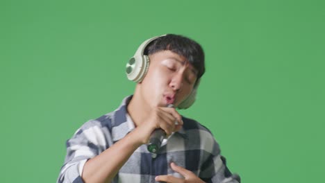 close up young asian teen boy holding a microphone and rapping on the the green screen background