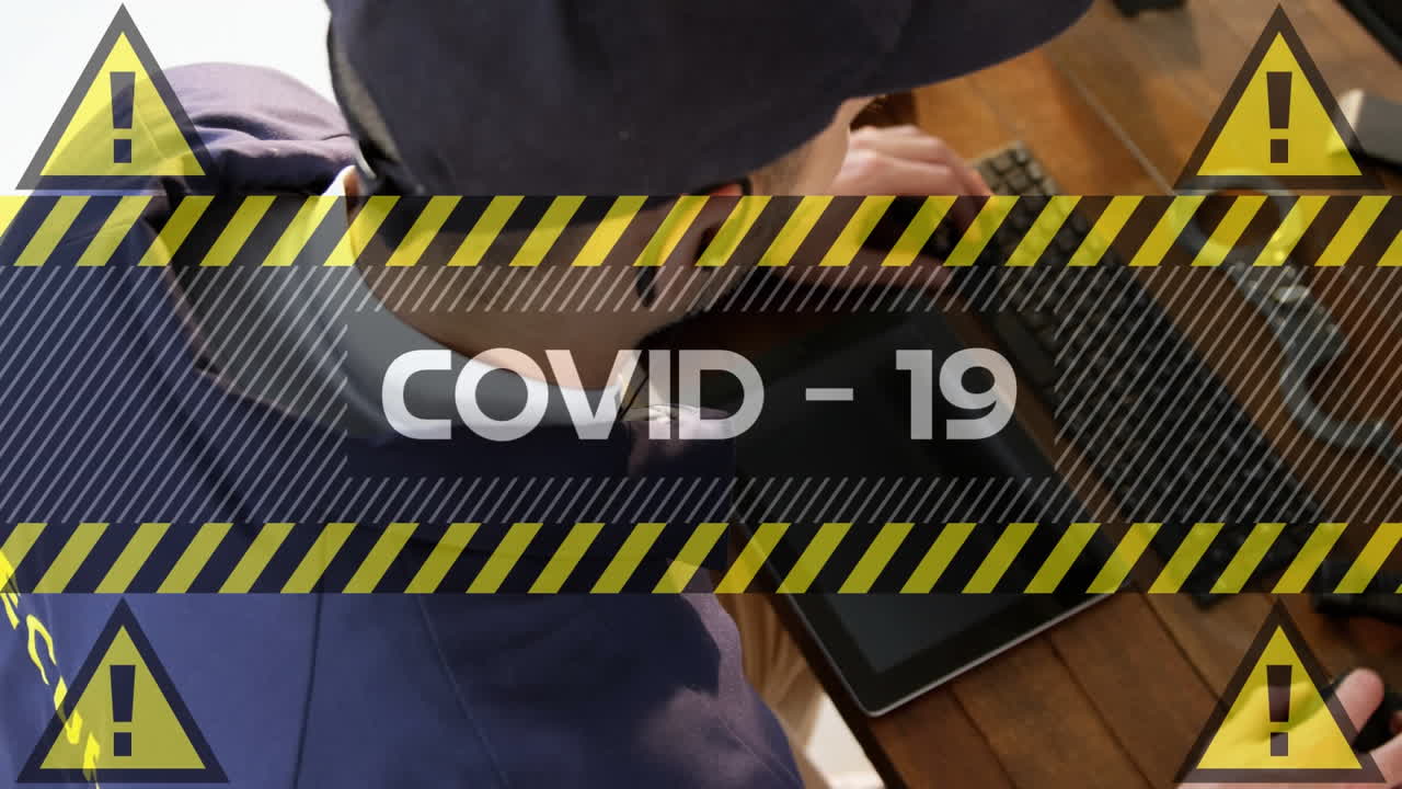 Video composito digitale di testo Covid-19 con un segnale di avvertimento giallo su uno sfondo di una guardia di sicurezza uomo che usa il computer.