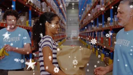 Animation-of-snowflakes-falling-over-diverse-volunteers-in-warehouse