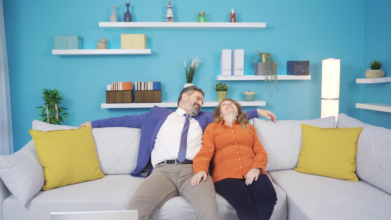 The man from work takes his wife's hand and they sit on the sofa.