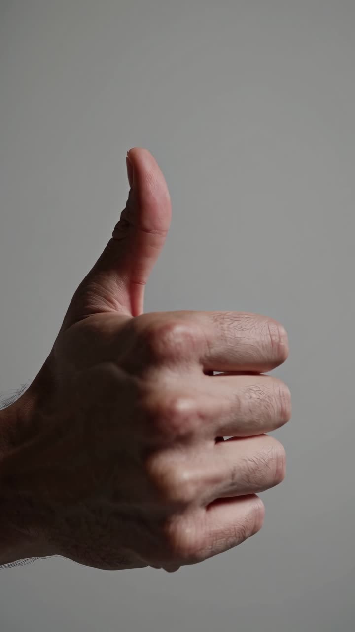 Video ravvicinato di una mano che fa il gesto del pollice in su su uno sfondo neutro.