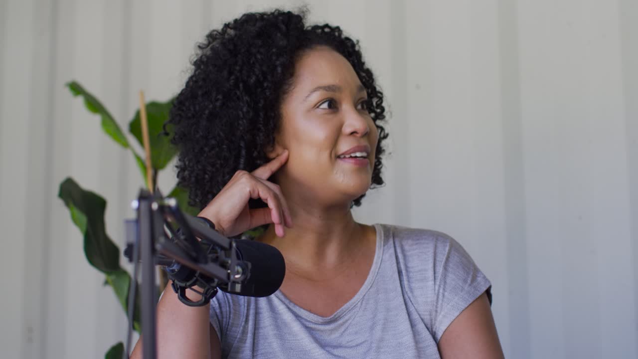 Afroamerikansk kvinde hører signal, justerer bommikrofon smilende, optager podcast i hjemmestudie