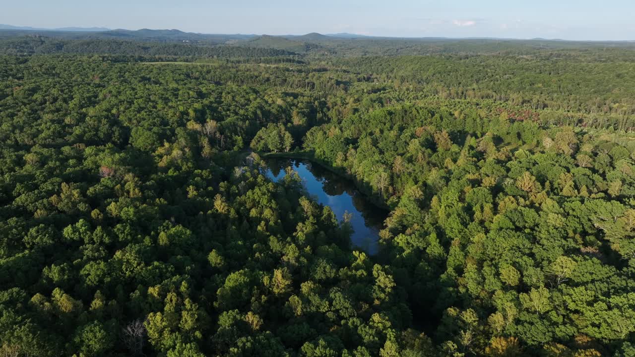 Lake surrounded by green forest and scenic landscape in USA. Aerial approaching descend shot. Sunny late summer season in suburb area of town