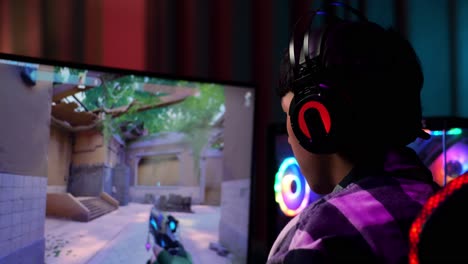 primer plano de un adolescente asiático emocionado que celebra la victoria mientras juega a videojuegos en la computadora, videojuegos de disparos en línea
