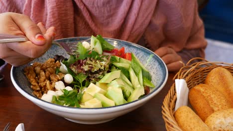 woman eating a salad with avocado, walnuts, cucumber, tomato, and mozzarella