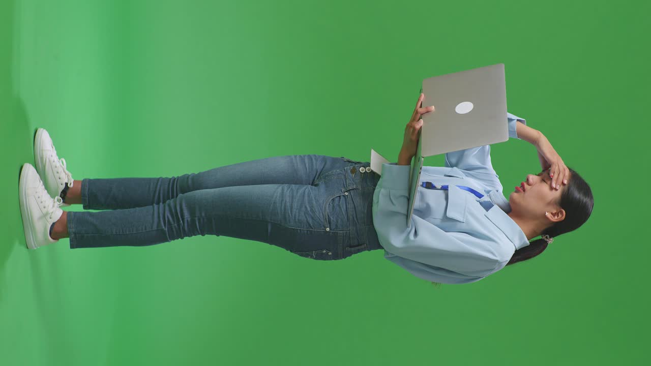 vista lateral de todo el cuerpo mujer de negocios asiática no está satisfecha y sacude la cabeza mientras usa la computadora portátil en el estudio de pantalla verde