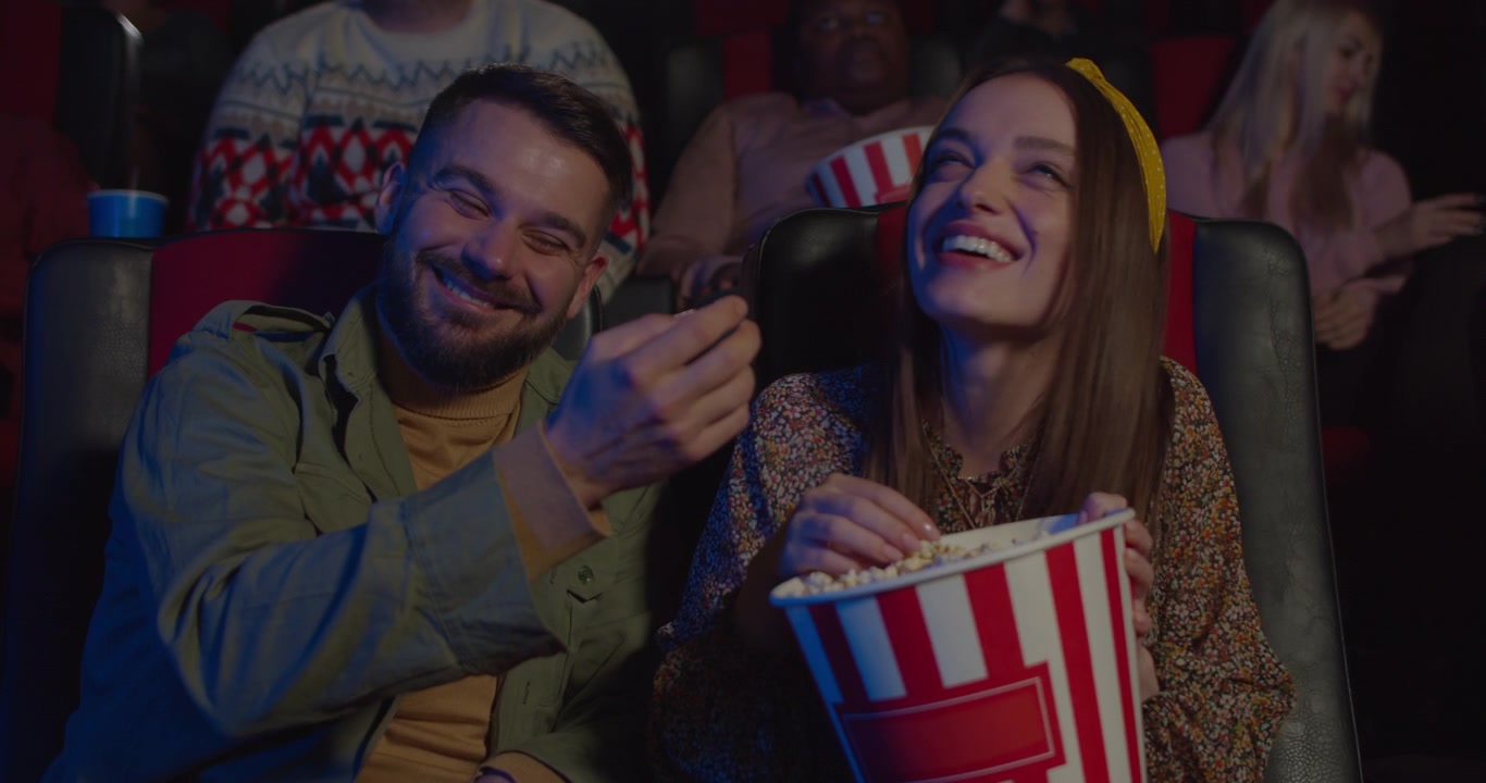 Pareja joven comiendo palomitas de maíz y riendo en el cine.
