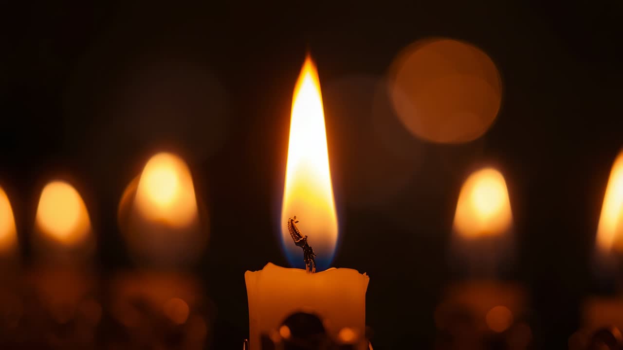 Opening on white pillar candle flame flickering in air currents in dim room, with bokeh lights