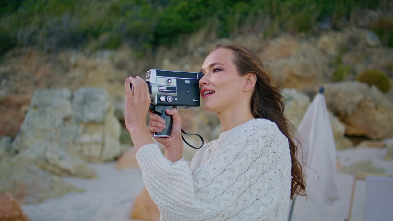 Girl holding retro camera on windy evening nature closeup. Young woman filming