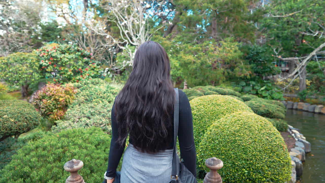 un video estabilizado en cámara lenta de 4k que representa a una hermosa joven modelo femenina de oriente medio explorando un exuberante jardín de té japonés caminando por un sendero del jardín, península, california