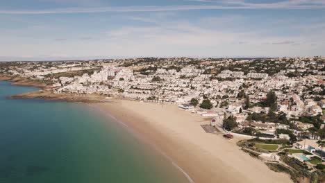 Peaceful-Algarve-beach,-calm-emerald-ocean-and-Praia-da-Luz-white-townhouses