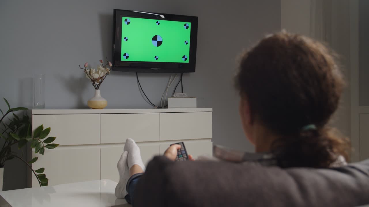 Sidelæns kamerabevægelse, kvinde ser tv derhjemme, greenscreen.