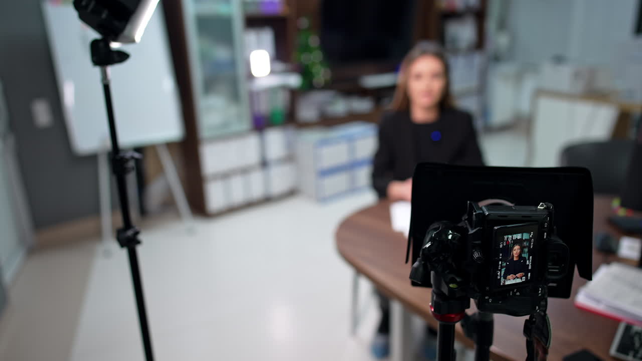 Camera on tripod recording a female speaking and gesturing. High angle view at equipment filming a blogger.