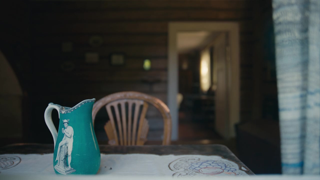 A vintage blue porcelain pitcher rests on an old table inside a dim historic room, where soft light, worn furniture, and quiet stillness create a nostalgic scene rich with memory.
