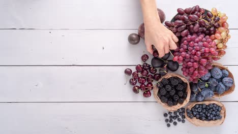 manos femeninas arreglando una gran selección de frutas en paneles de madera blanca. colorido de acción de gracias o concepto de cosecha..