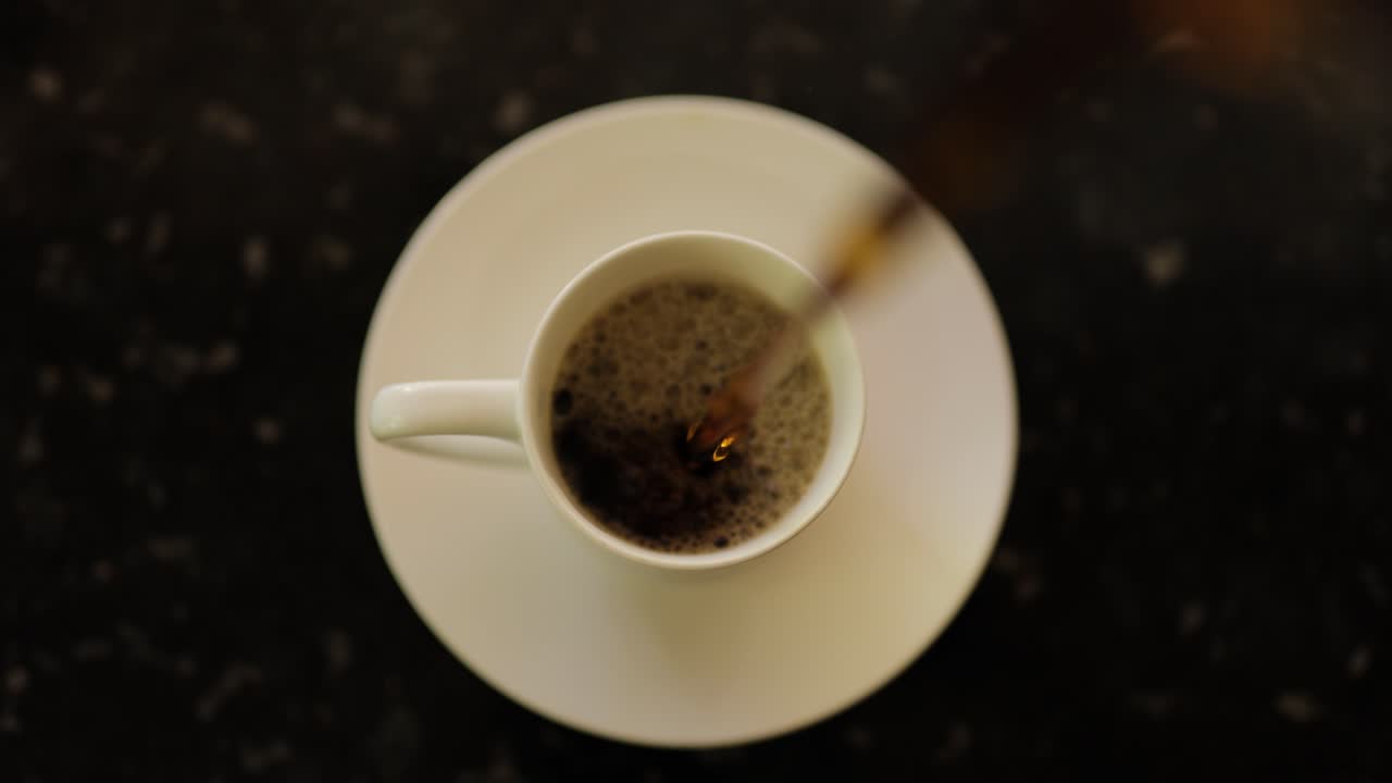 primo piano vista a volo d'uccello del caffè che si versa in una tazza di caffè su un piatto sul piano di lavoro