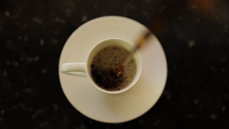 close up birds eye view of coffee pouring into a coffee cup on a dish on countertop