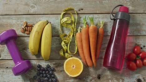 video de frutas frescas, cinta métrica, botella de agua y pesas en tablas de madera