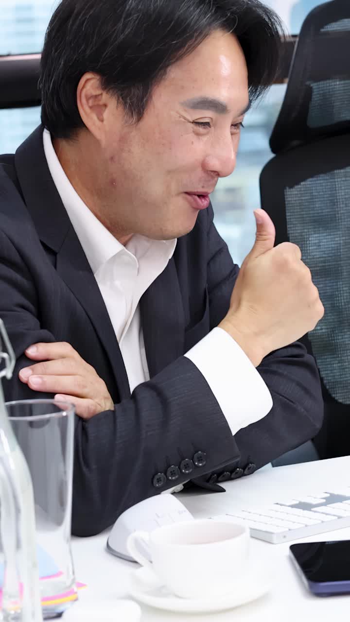 Một doanh nhân châu Á mỉm cười và giơ ngón tay cái lên trong cuộc họp văn phòng sáng sủa.