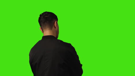 Rear-View-Of-Bored-Or-Fed-Up-Young-Man-Standing-And-Waiting-Against-Green-Screen-Background