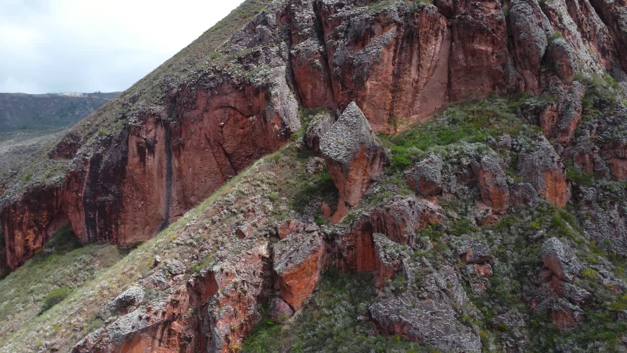 Ilmakuvaus dronella, jossa pannauskuva Andien vuoriston punertavista kalliojyrkänteistä. Kuvaus vangitsee karut yksityiskohdat, geologiset tekstuurit ja valtavan mittakaavan Oñassa, Ecuadorissa.