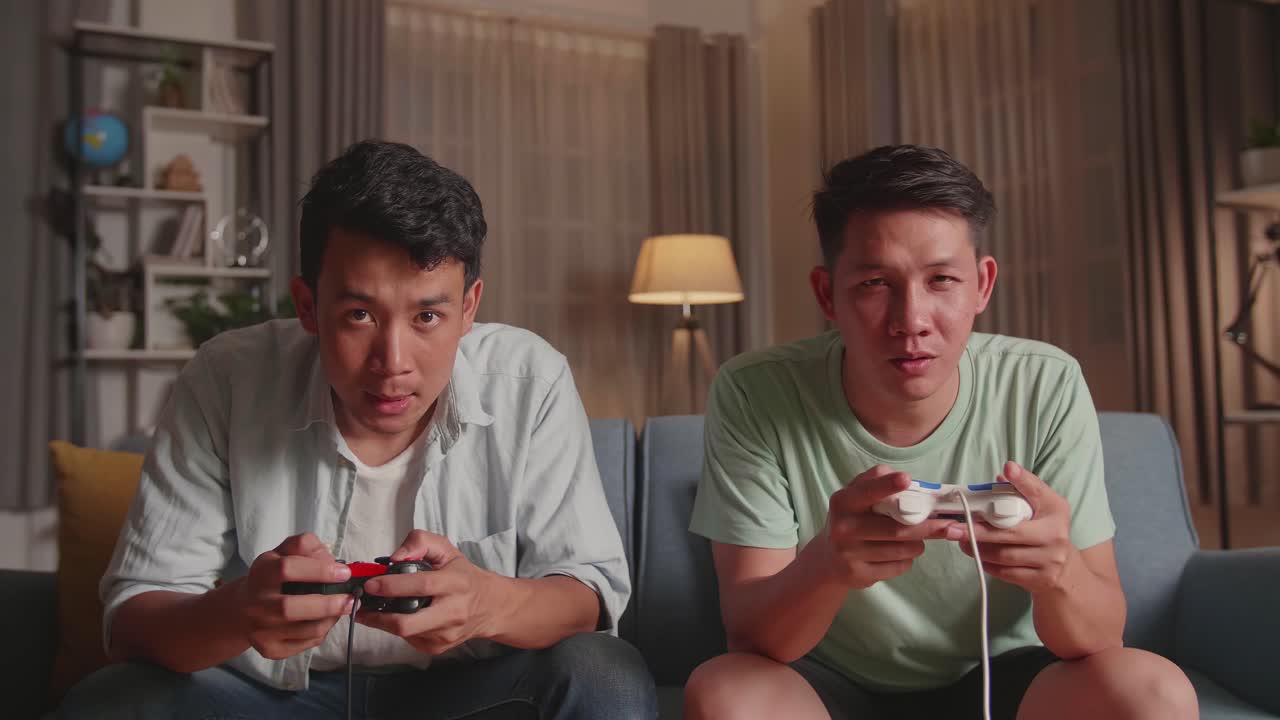 Asian Friends Playing Video Games At Home. Male Happy To Win Victory And Another Man Feeling Disappointed