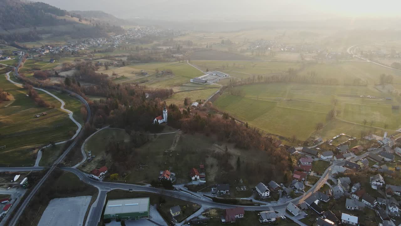 Drone orbiting over Church of St. Andrew at dawn in green Bled valley Slovenia