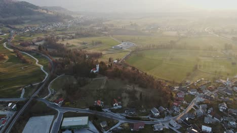 drone orbiting over church of st. andrew at dawn in green bled valley slovenia