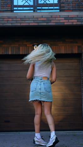 woman wearing white shirt, jeans mini skirt and sunglasses poses outdoors. lady comes up to camera, squats in front of it. baby boy runs up to mom. vertical video