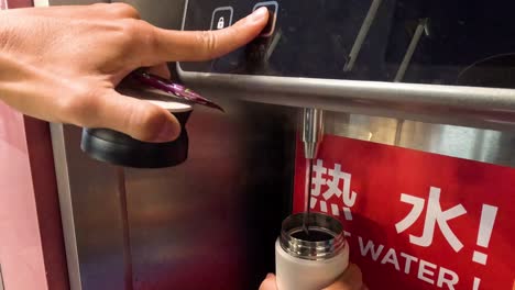 person fills thermos from hot water dispenser