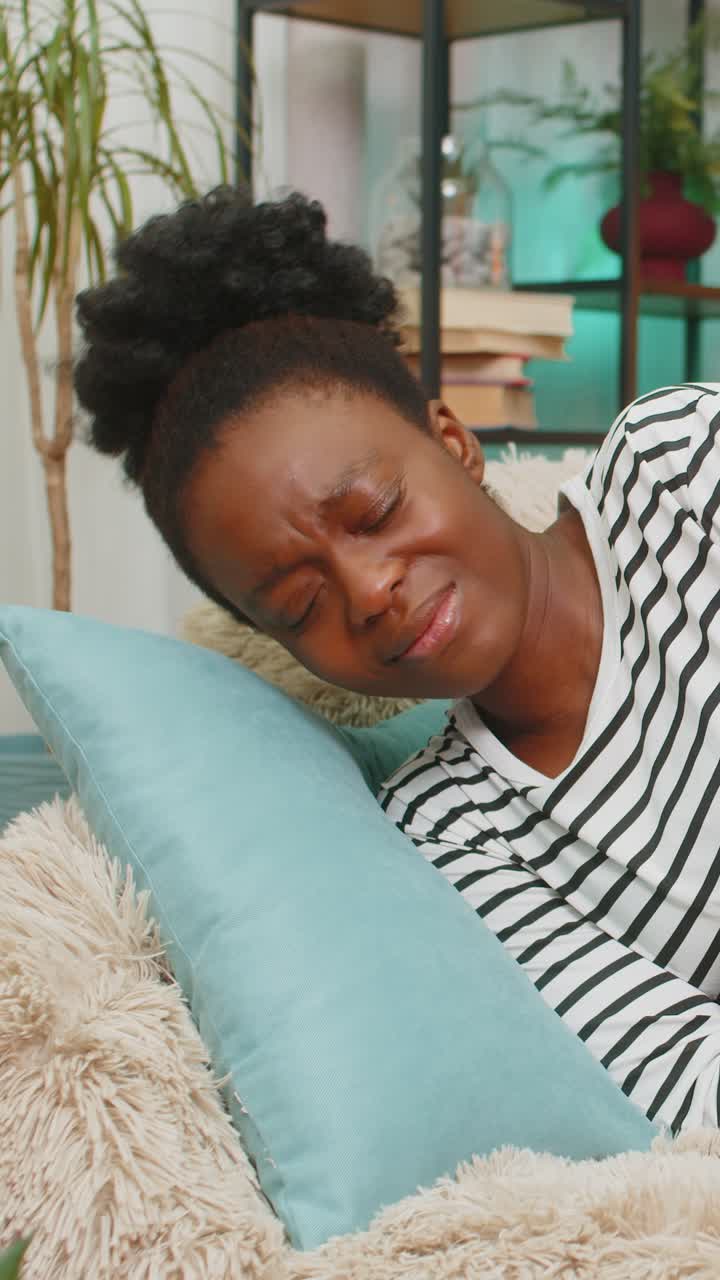African american woman feeling stomach pain holding abdomen lying exhausted on couch indoors