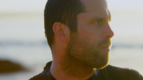 close-up of mid-adult caucasian male surfer standing at beach during sunset 4k