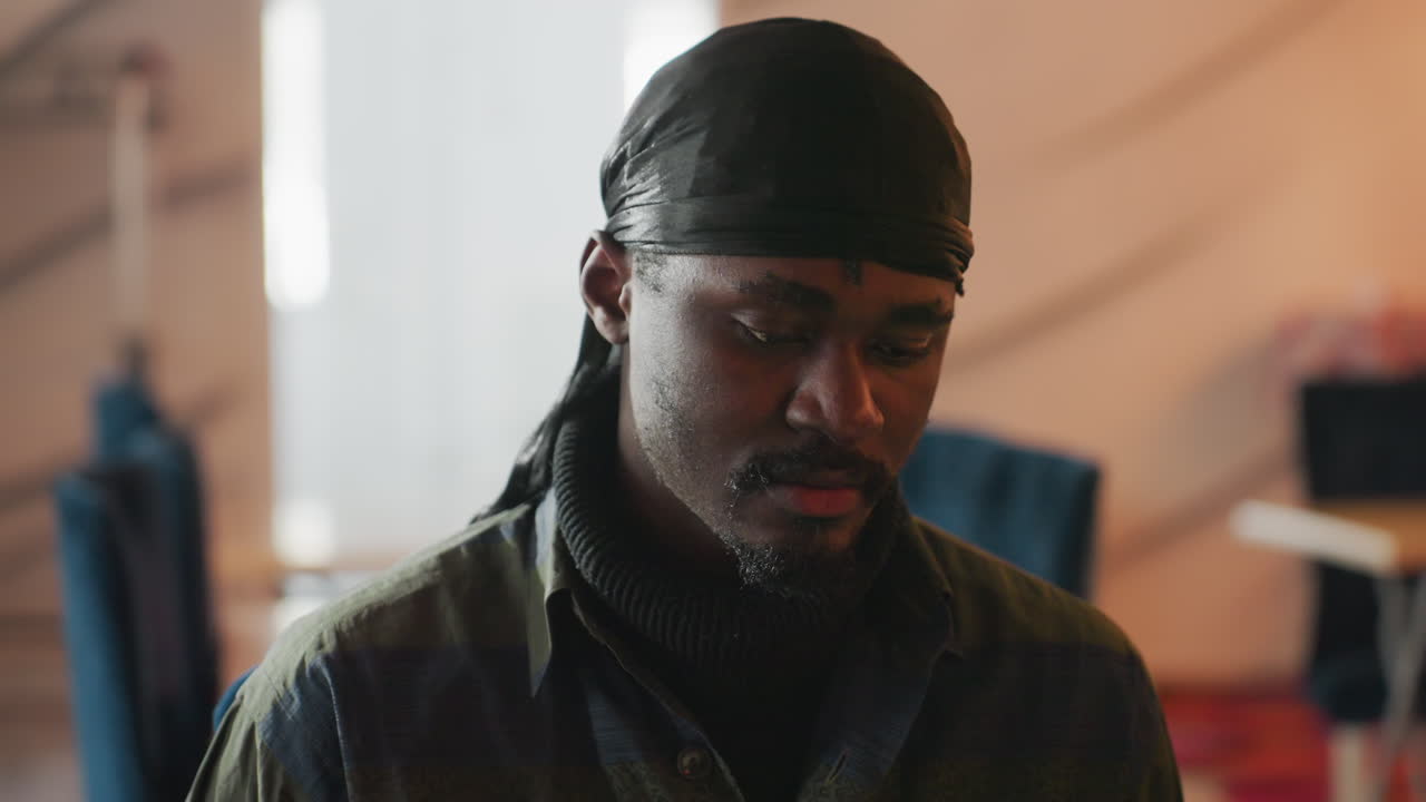 Крупный план задумчивого художника: выразительные глаза отражают глубокую интроспекцию в студии, крупный план интроспективного афроамериканского художника с мягким освещением и тонкими выражениями лица