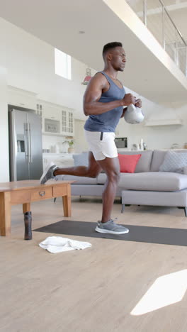hombre afroamericano concentrado haciendo ejercicio con kettlebell en la sala de estar soleada, cámara lenta