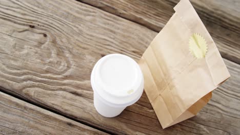 taza de café desechable y paquete en tabla de madera